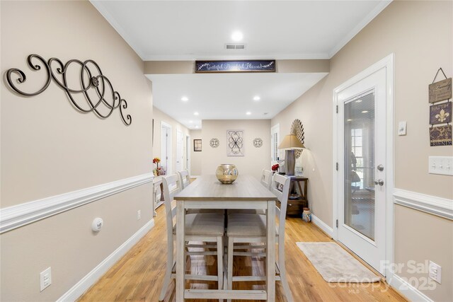 dining area with visible vents, baseboards, crown molding, and light wood-style floors