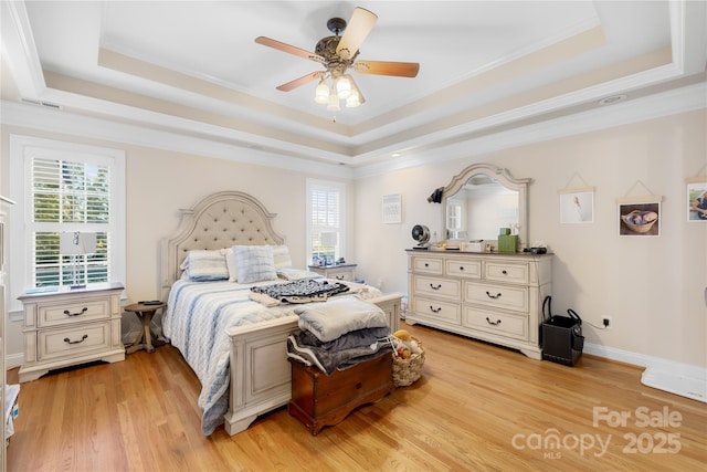 bedroom featuring a raised ceiling, multiple windows, and light wood-style floors