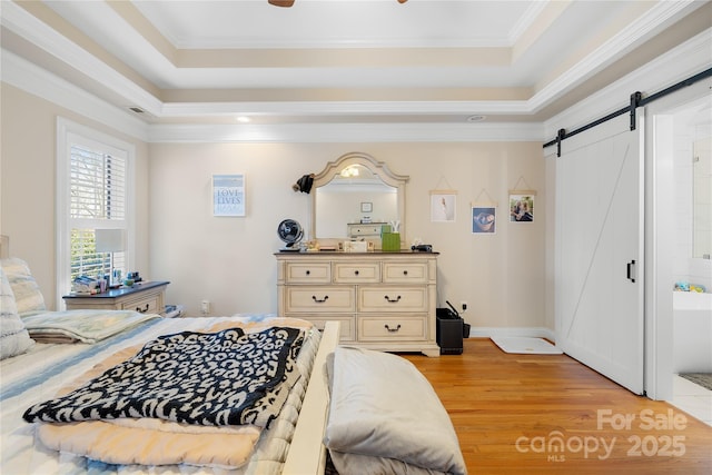 bedroom featuring baseboards, light wood-type flooring, a tray ceiling, a barn door, and ornamental molding