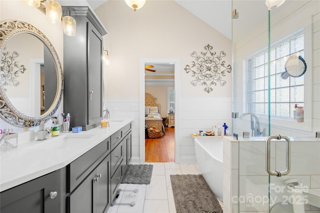 bathroom with a wainscoted wall, vanity, lofted ceiling, a bathtub, and ensuite bath