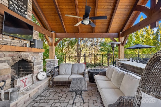 view of patio featuring a ceiling fan, an outdoor living space with a fireplace, and fence