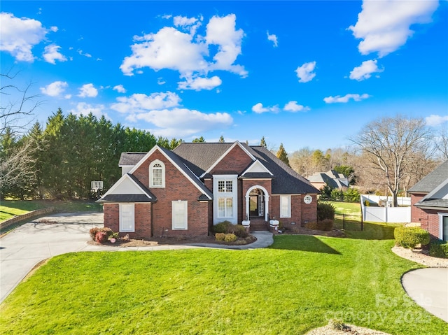 traditional-style home featuring driveway, a front lawn, fence, and brick siding