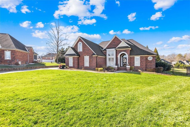 view of front of house featuring brick siding, roof with shingles, a front yard, and fence