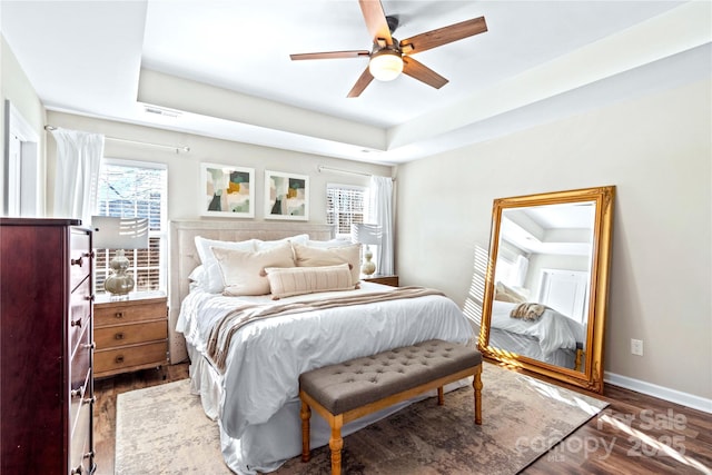 bedroom with a raised ceiling, ceiling fan, dark hardwood / wood-style flooring, and multiple windows