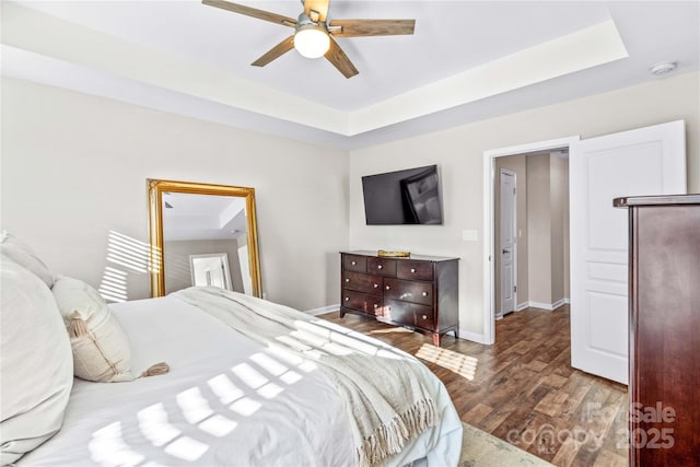 bedroom with ceiling fan, hardwood / wood-style floors, and a tray ceiling