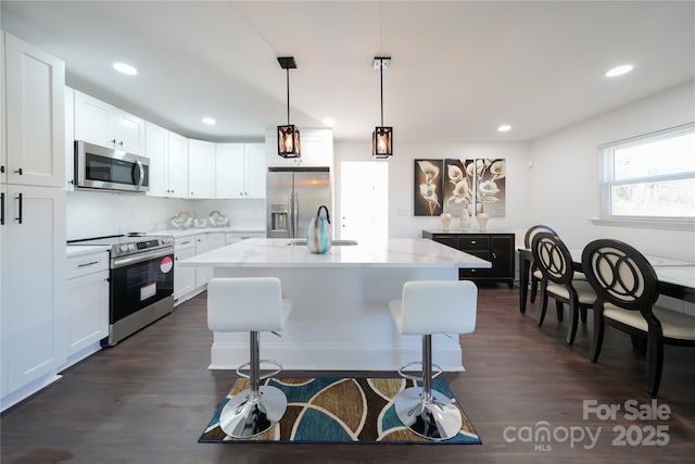 kitchen featuring decorative light fixtures, white cabinets, stainless steel appliances, and an island with sink