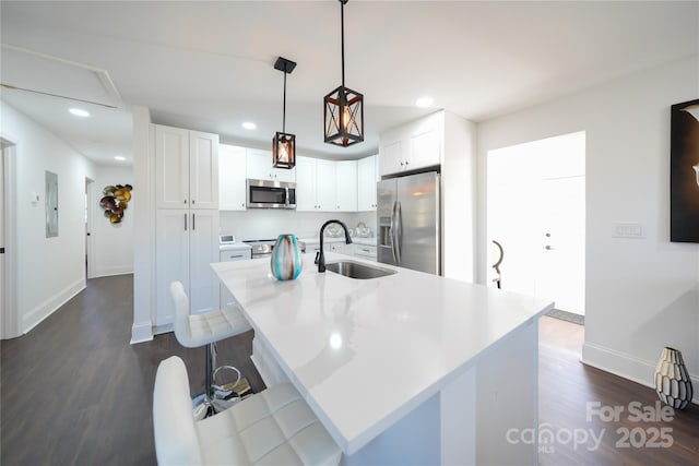 kitchen with decorative light fixtures, sink, an island with sink, stainless steel appliances, and white cabinets