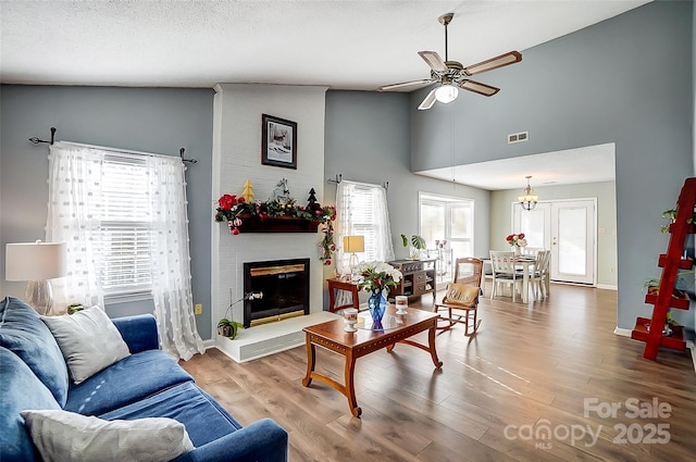 living room with a large fireplace, hardwood / wood-style flooring, a textured ceiling, high vaulted ceiling, and ceiling fan with notable chandelier