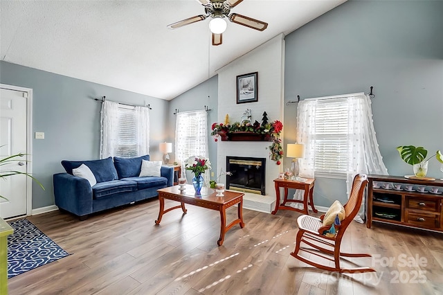 living room with ceiling fan, a fireplace, hardwood / wood-style flooring, and high vaulted ceiling