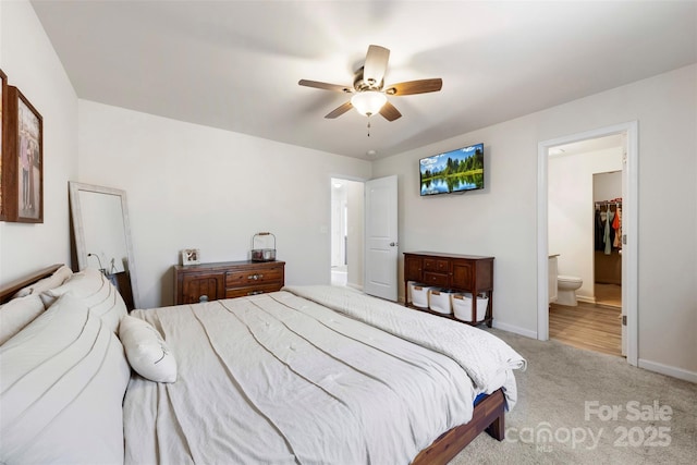 bedroom with connected bathroom, a closet, light colored carpet, ceiling fan, and a spacious closet