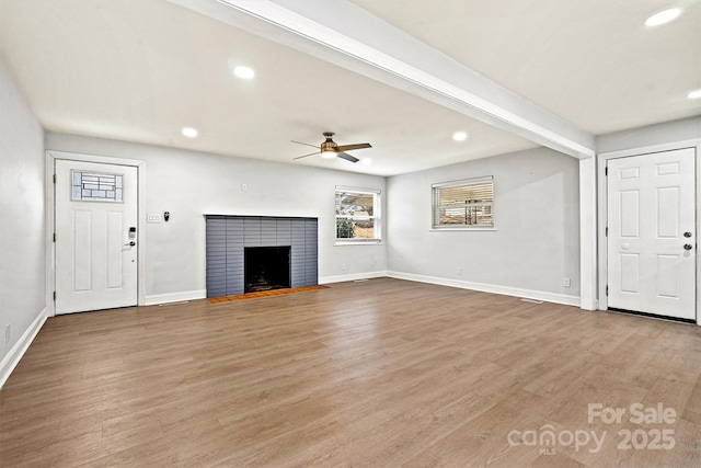 unfurnished living room with a tile fireplace, wood-type flooring, ceiling fan, and beamed ceiling