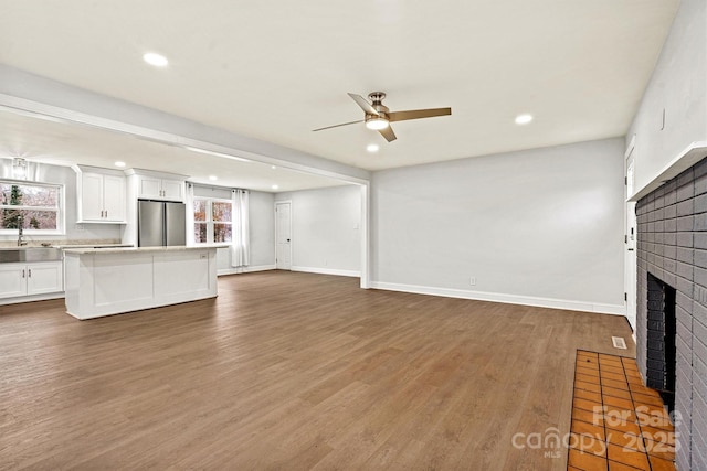 unfurnished living room with dark hardwood / wood-style flooring, a brick fireplace, sink, and ceiling fan