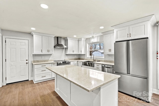 kitchen with sink, white cabinetry, stainless steel appliances, a kitchen island, and wall chimney exhaust hood