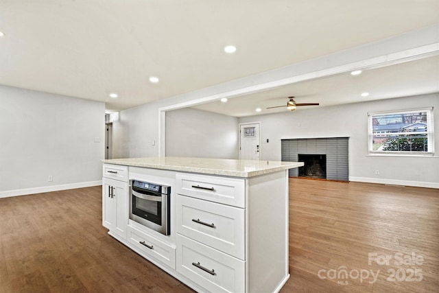 kitchen with white cabinetry, stainless steel oven, light stone counters, and light hardwood / wood-style flooring