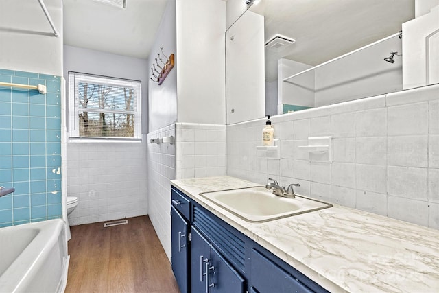 full bathroom with tile walls, hardwood / wood-style floors, vanity, shower / bathing tub combination, and toilet