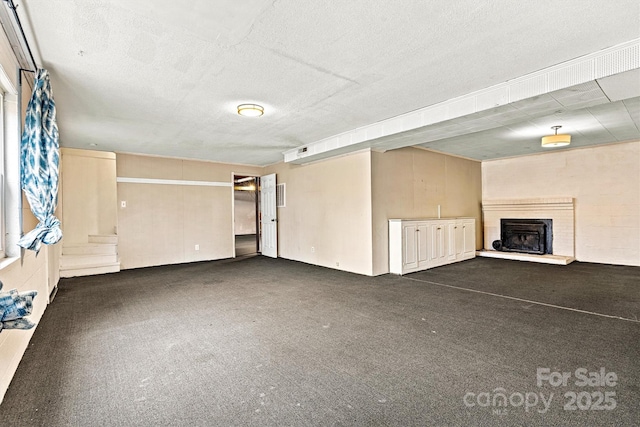 unfurnished living room featuring dark colored carpet and a textured ceiling