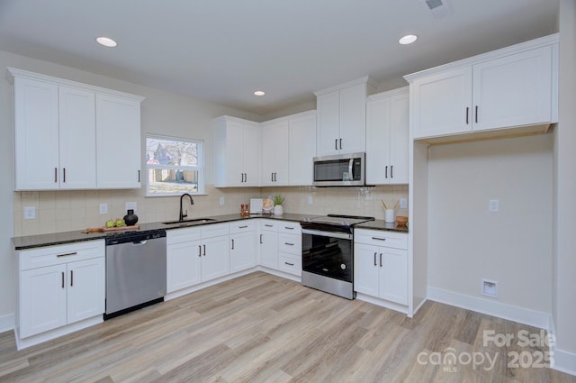 kitchen with sink, white cabinetry, light hardwood / wood-style flooring, decorative backsplash, and appliances with stainless steel finishes