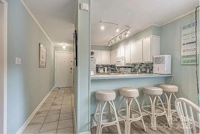 kitchen with white cabinets, white appliances, light tile patterned floors, kitchen peninsula, and decorative backsplash