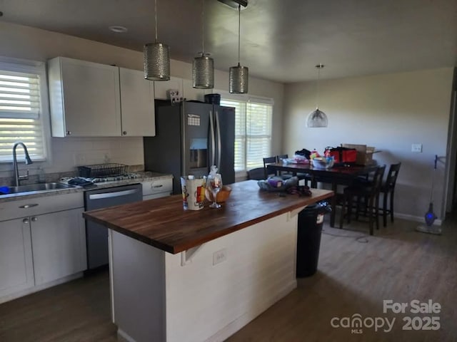 kitchen featuring butcher block counters, a kitchen island, a sink, appliances with stainless steel finishes, and pendant lighting