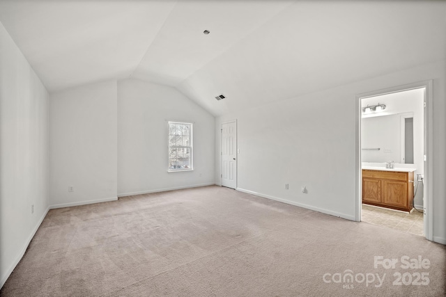 interior space with ensuite bathroom, vaulted ceiling, light carpet, and sink