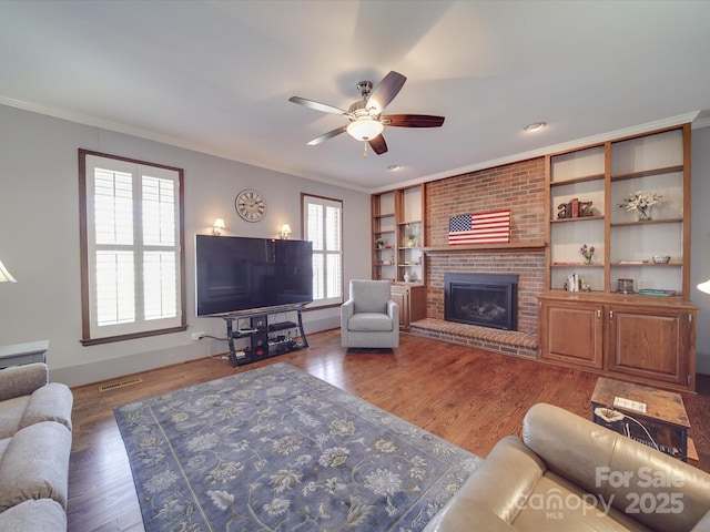 living room featuring a brick fireplace, crown molding, dark wood-type flooring, and ceiling fan