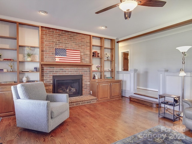 living room featuring built in features, hardwood / wood-style flooring, ceiling fan, crown molding, and a brick fireplace