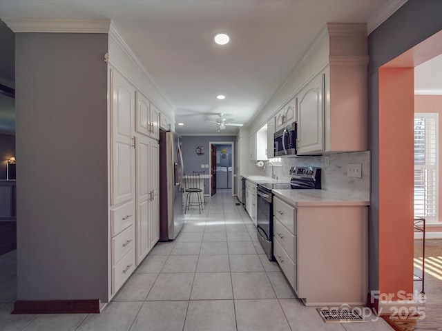 kitchen featuring tasteful backsplash, crown molding, white cabinets, and appliances with stainless steel finishes