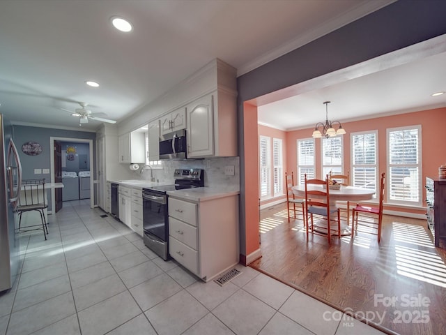 kitchen with white cabinetry, stainless steel appliances, ornamental molding, separate washer and dryer, and decorative light fixtures