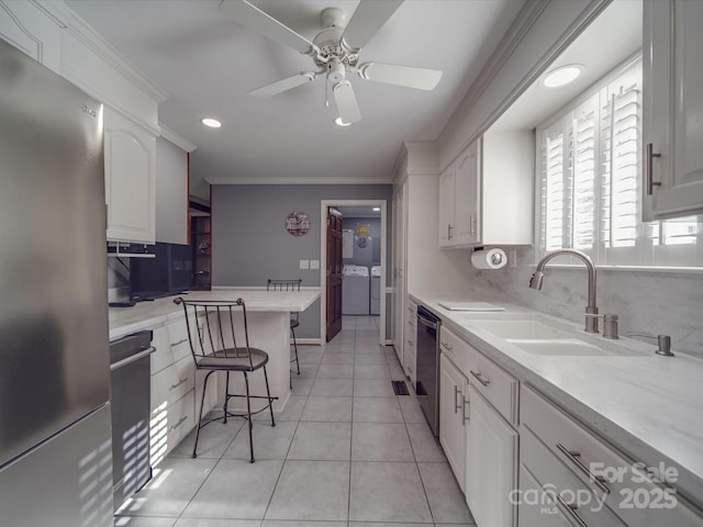 kitchen featuring stainless steel appliances, ornamental molding, washer and dryer, white cabinets, and a kitchen bar