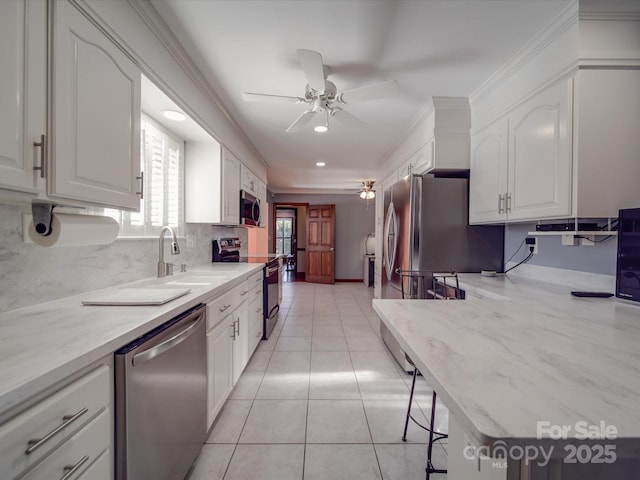 kitchen featuring sink, light tile patterned floors, stainless steel appliances, ornamental molding, and white cabinets