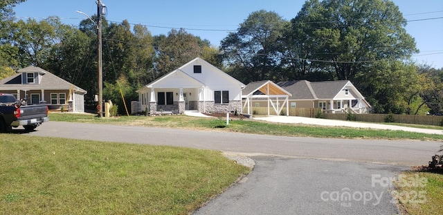 bungalow featuring covered porch, fence, stone siding, driveway, and a front yard