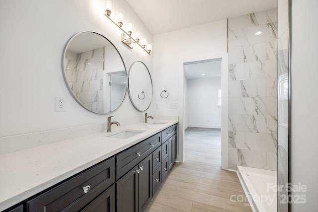 full bath featuring wood finished floors, a sink, a marble finish shower, and double vanity