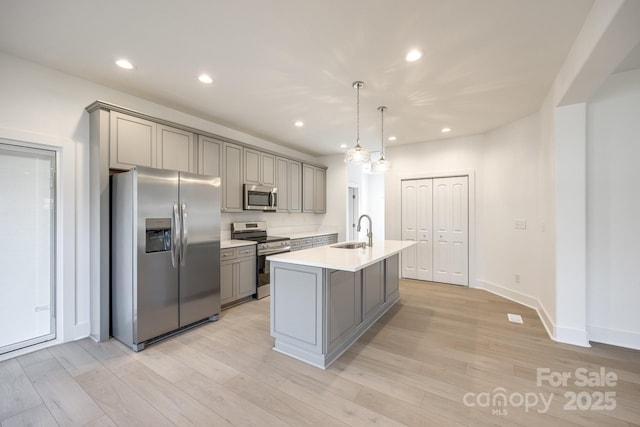 kitchen featuring a center island with sink, gray cabinets, light countertops, hanging light fixtures, and appliances with stainless steel finishes