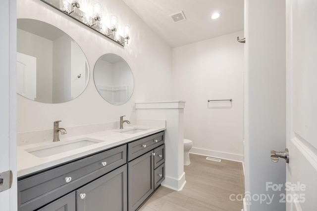 bathroom with toilet, double vanity, a sink, and visible vents