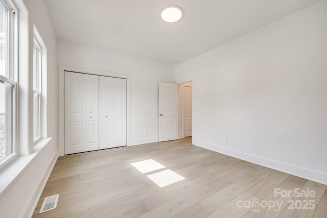 unfurnished bedroom featuring light wood-style floors, visible vents, baseboards, and multiple windows