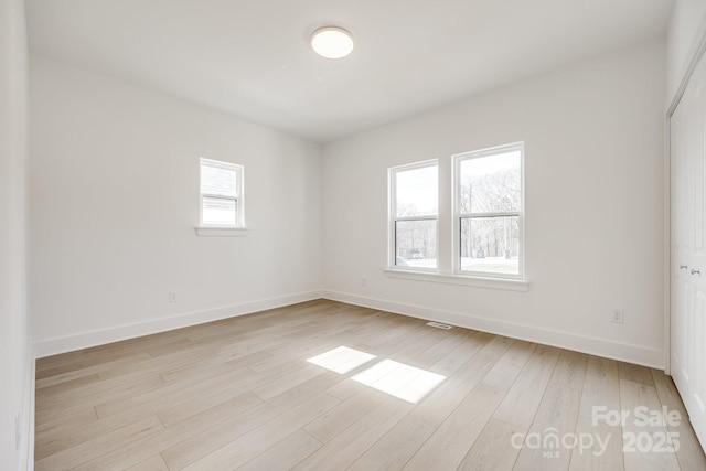 spare room with light wood finished floors, visible vents, and baseboards