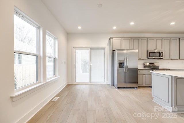 kitchen with gray cabinetry, stainless steel appliances, visible vents, light countertops, and light wood finished floors