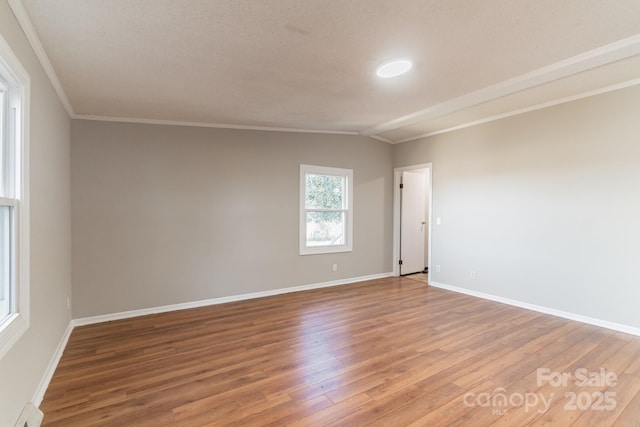 empty room featuring lofted ceiling, wood-type flooring, baseboard heating, and crown molding