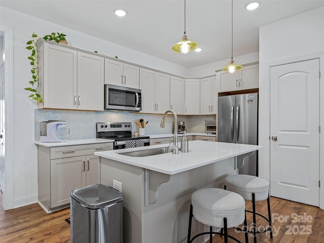 kitchen featuring an island with sink, appliances with stainless steel finishes, dark hardwood / wood-style floors, hanging light fixtures, and sink