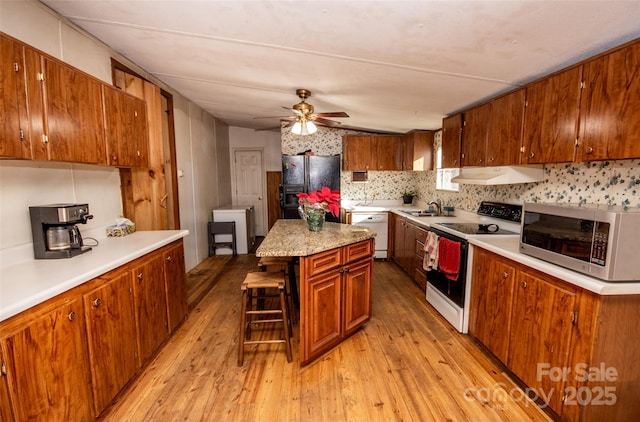 kitchen with white appliances, a center island, light hardwood / wood-style floors, a kitchen bar, and sink