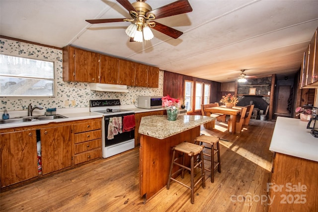 kitchen featuring electric stove, a breakfast bar, a kitchen island, light wood-type flooring, and sink