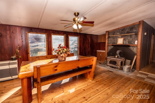 dining room with vaulted ceiling, light hardwood / wood-style floors, ceiling fan, wooden walls, and a wood stove