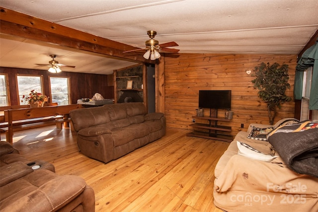 living room featuring ceiling fan, light wood-type flooring, wooden walls, and lofted ceiling with beams