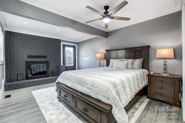 bedroom featuring ceiling fan, a brick fireplace, crown molding, light hardwood / wood-style flooring, and beamed ceiling