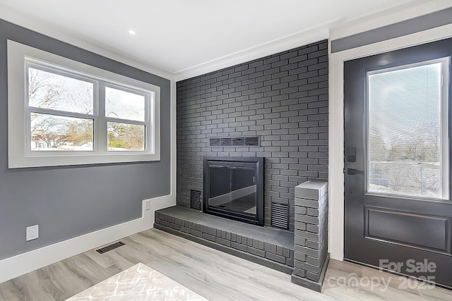 interior space with wood-type flooring, a brick fireplace, and ornamental molding