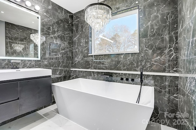 bathroom with an inviting chandelier, tile walls, a tub to relax in, and vanity