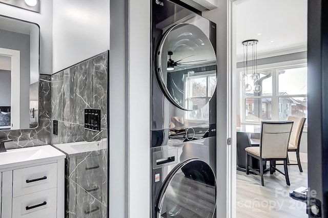 laundry area with stacked washing maching and dryer, plenty of natural light, sink, and crown molding