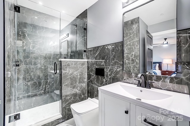 bathroom with a shower with shower door, vanity, tile walls, toilet, and ceiling fan