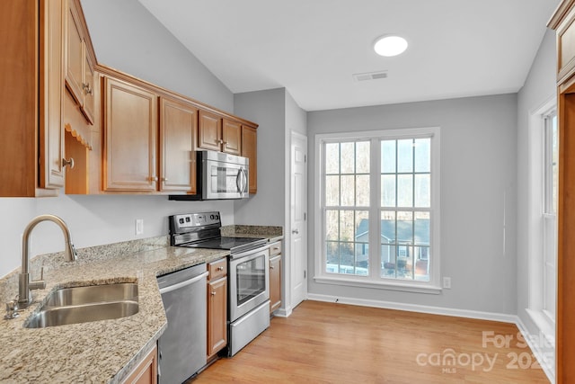 kitchen with light stone countertops, vaulted ceiling, light hardwood / wood-style flooring, stainless steel appliances, and sink