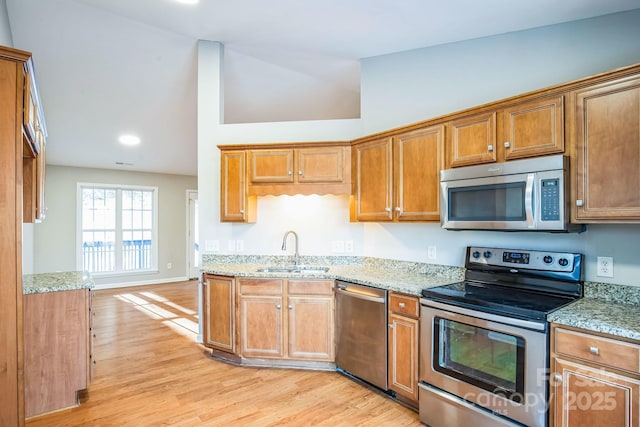 kitchen with stainless steel appliances, sink, vaulted ceiling, light wood-type flooring, and light stone countertops